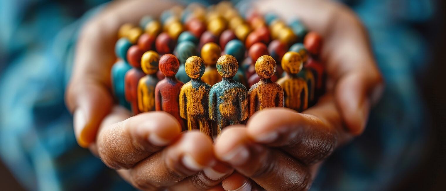Zu einer Schale geformte Hände halten im Kreis eng zusammenstehenden Personen-Figuren aus Holz, die bunten Farben blättern ab