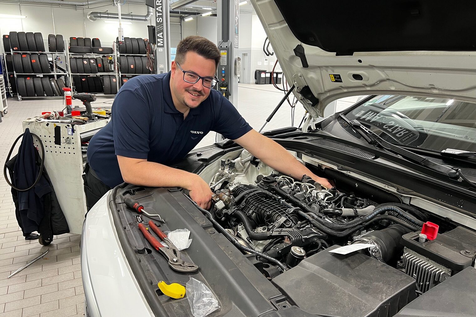 Mann greift in Motorhaube von Auto und lächelt in die Kamera.