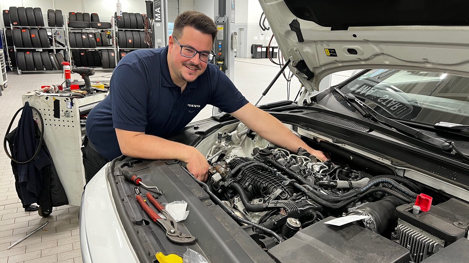 Mann greift in Motorhaube von Auto und lächelt in die Kamera.