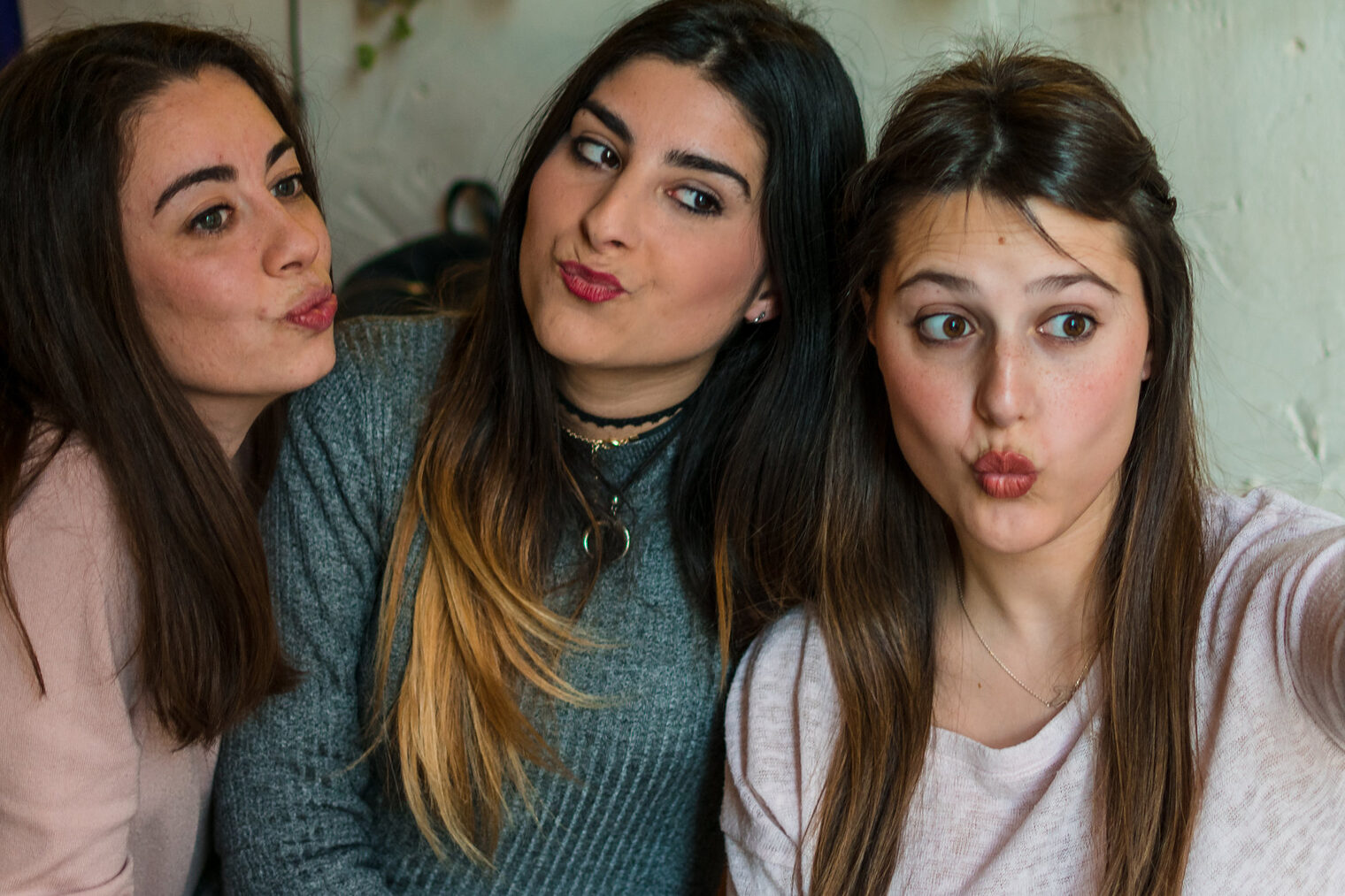 Drei jugendliche Frauen sitzen auf einem Sofa und posen in das Handy, das das rechte Mädchen für ein Selfie vor sich hält. Alle machen einen Kussmund.