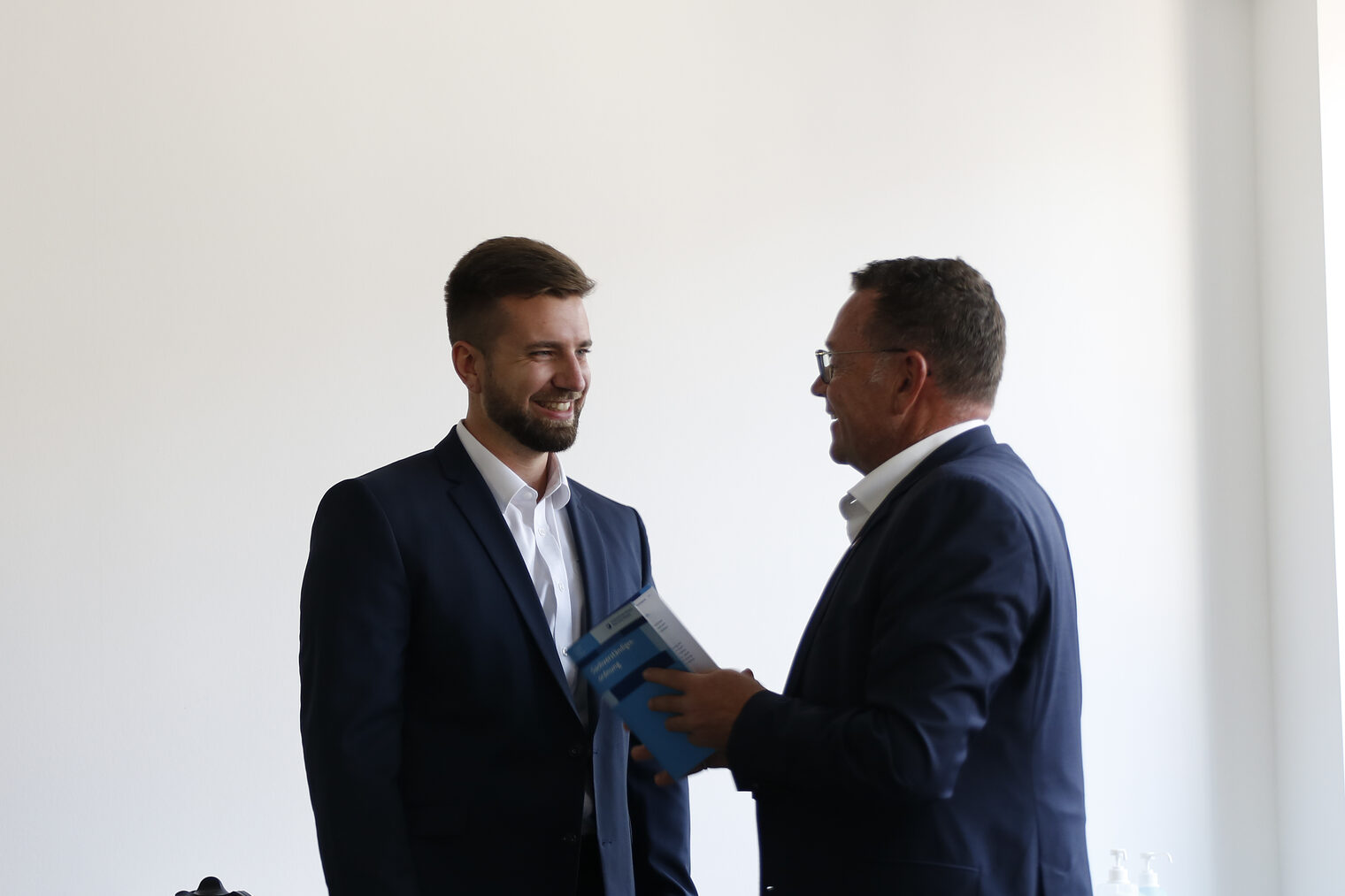 Mann in Anzug, der rechts steht, gratuliert jungem Mann links zum Amt des Sachverständigen.