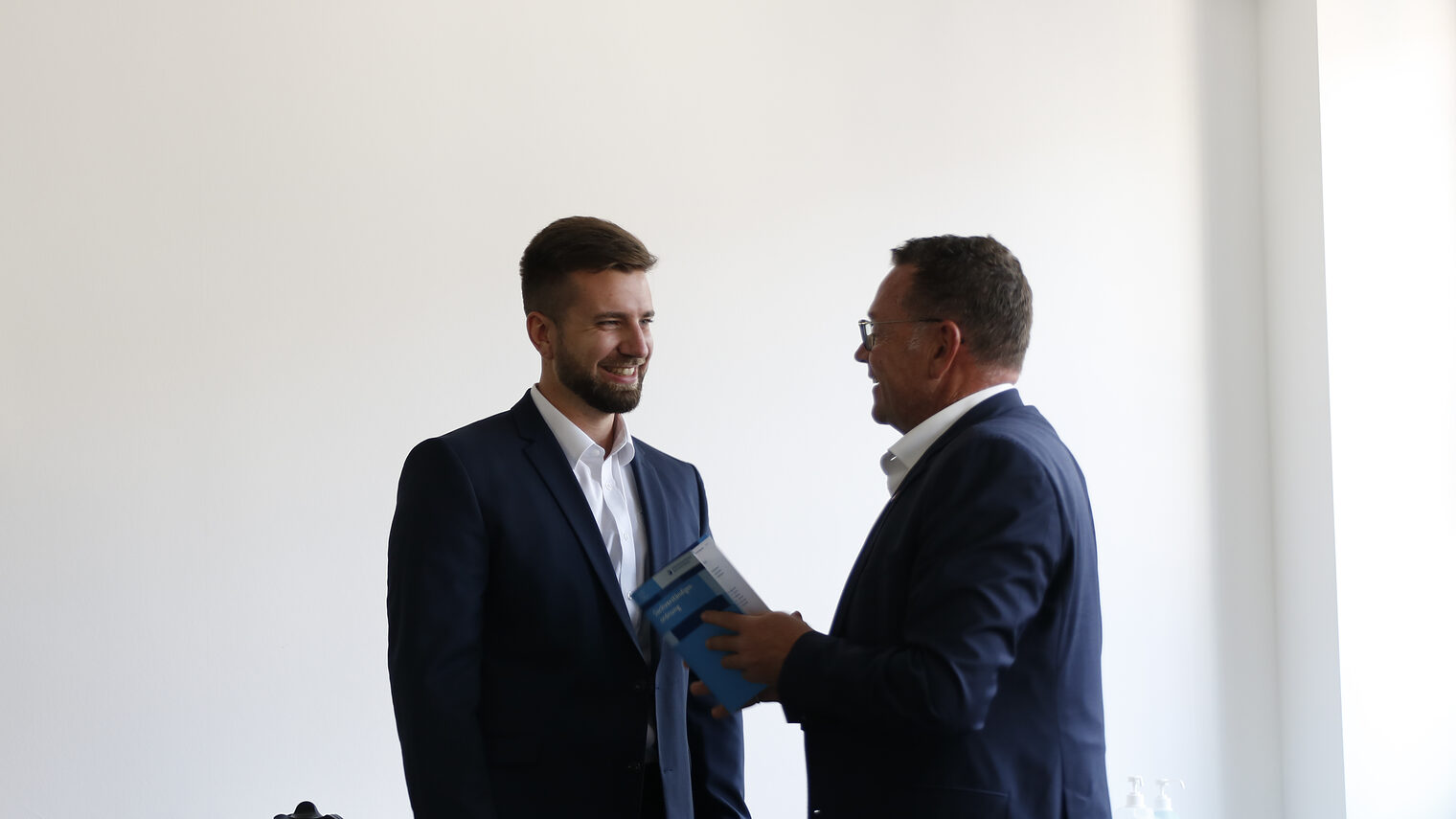 Mann in Anzug, der rechts steht, gratuliert jungem Mann links zum Amt des Sachverständigen.