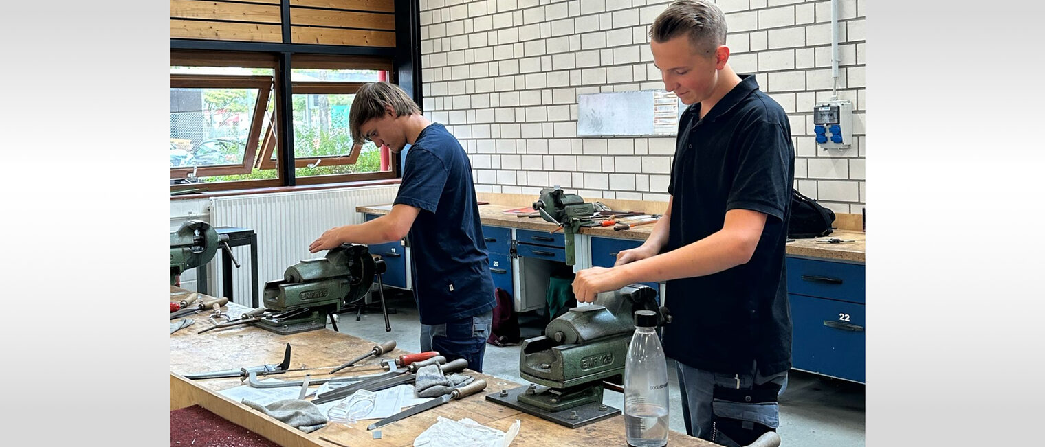 Zwei Jungs stehen vor einem Tisch und arbeiten an einer Maschine. 