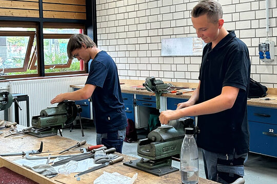 Zwei Jungs stehen vor einem Tisch und arbeiten an einer Maschine. 