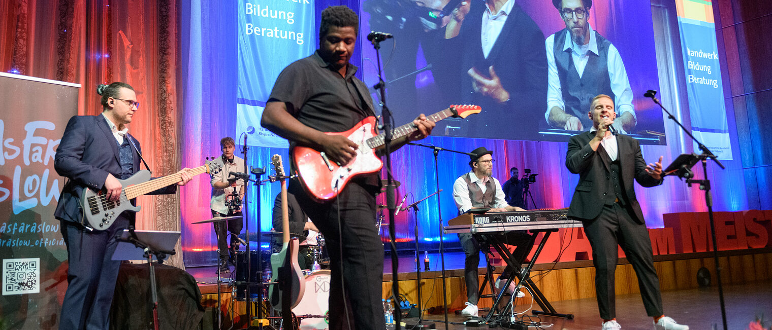 Man sieht 5 Personen die auf der Bühne stehen und Instrumente halten