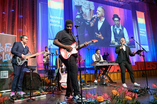 Man sieht 5 Personen die auf der Bühne stehen und Instrumente halten