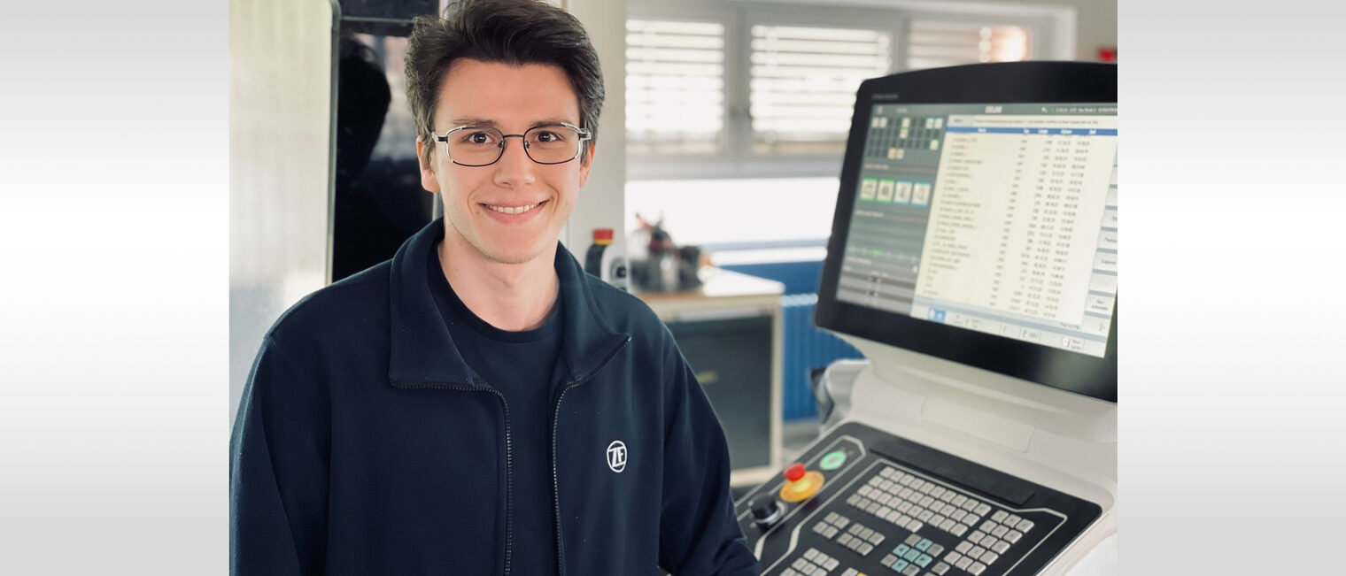 Meistergeschichte von Feinwerkmechaniker Floris Kalthoff Junger Mann sitzt vor technischem Gerät und lächelt in die Kamera.