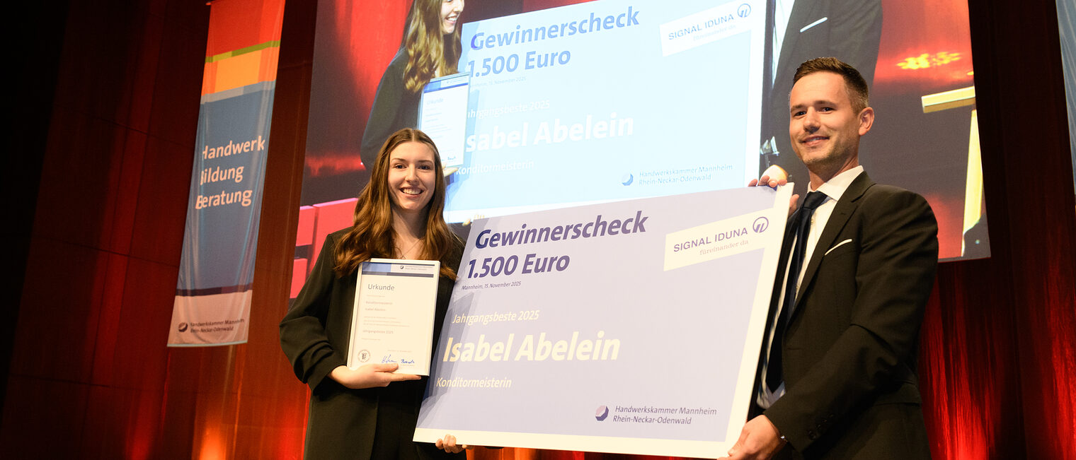 Zwei Personen stehen auf einer Bühne und halten zwischen Ihnen einen großen Scheck