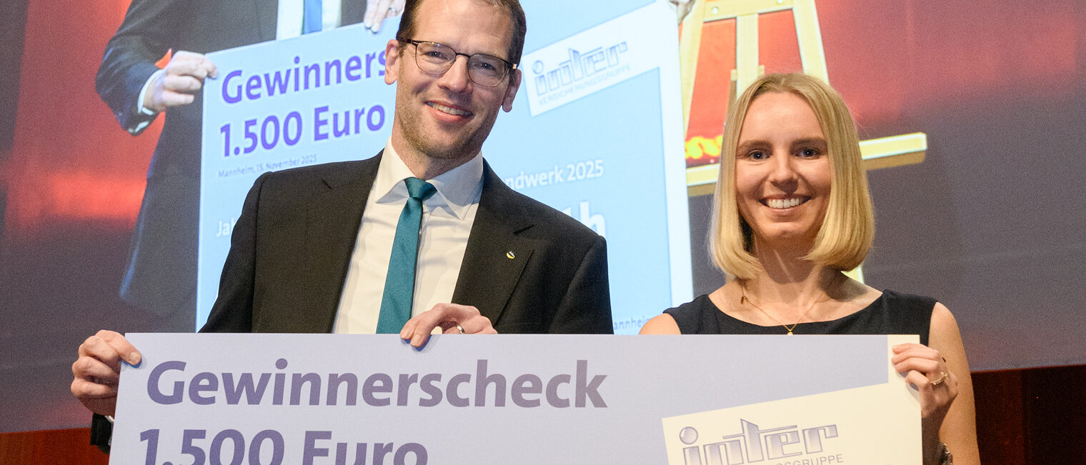 Zwei Personen stehen auf einer Bühne und halten einen sehr großen Scheck zusammen