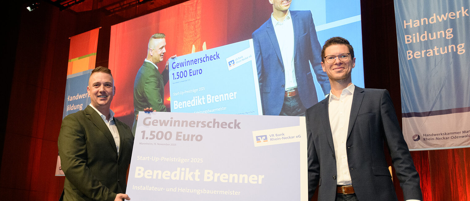 Zwei Personen stehen auf der Bühne und sie halten zusammen einen sehr großen Scheck