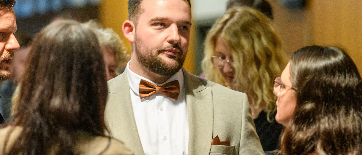 Ein Mann mit Anzug und Fliege hält seinen Meisterbrief in der Hand