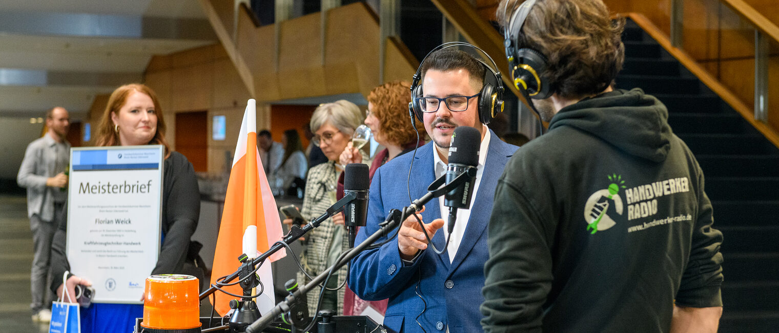 Zwei Männer stehen an einem mobilen Podcast Studio und haben Kopfhörer auf uns sprechen je in ein Mikrofon