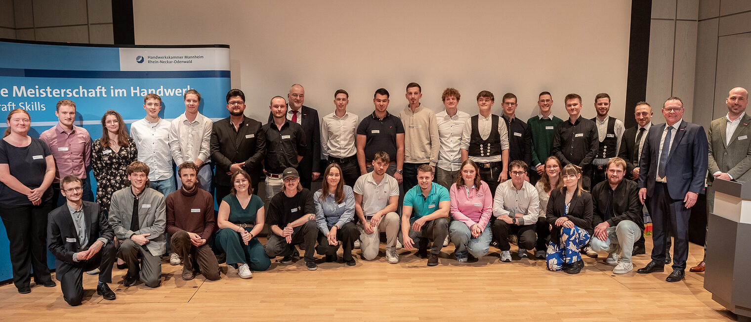 Eine Gruppe von Menschen in festlicher Kleidung posiert für ein Gruppenfoto, schauen in die Kamera. 