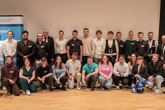 Eine Gruppe von Menschen in festlicher Kleidung posiert für ein Gruppenfoto, schauen in die Kamera. 