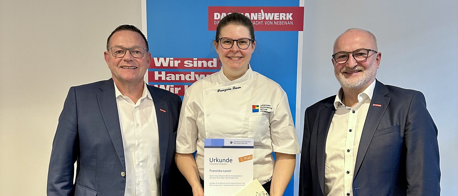 Drei Personen stehen mit dem Rücken zur Wand, die Preisträgerin in der Mitte hält ihren Preis in der Hand