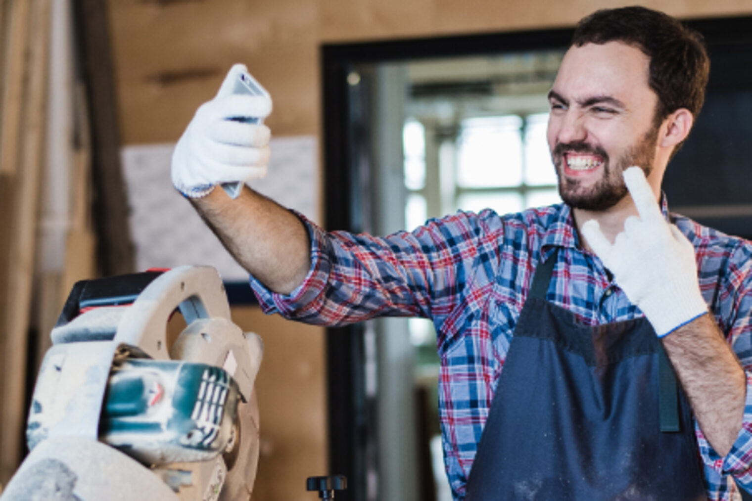Ein Handwerker macht in einer Werkstatt mit einem Smartphone ein Bild von sich selbst