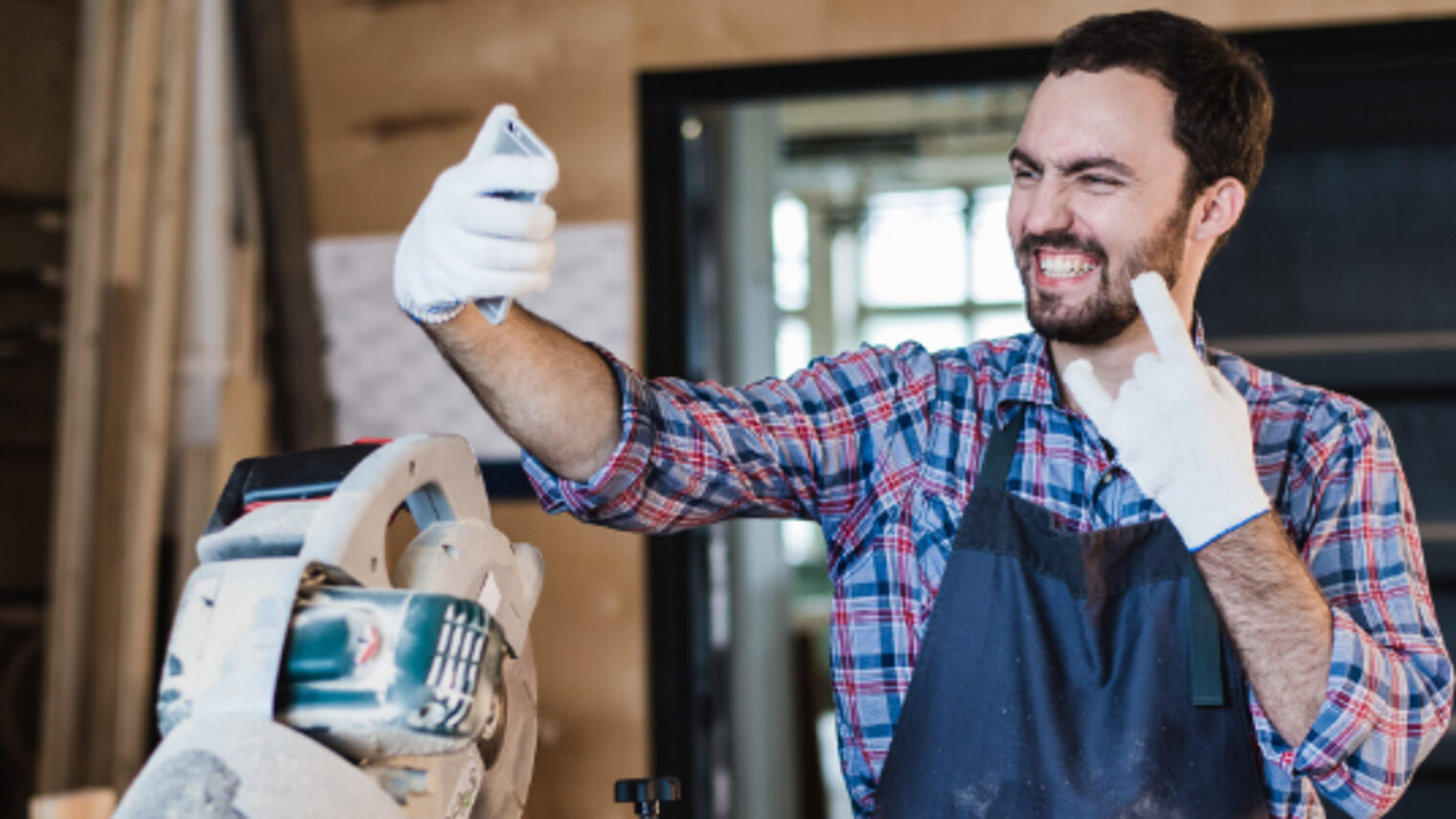 Ein Handwerker macht in einer Werkstatt mit einem Smartphone ein Bild von sich selbst