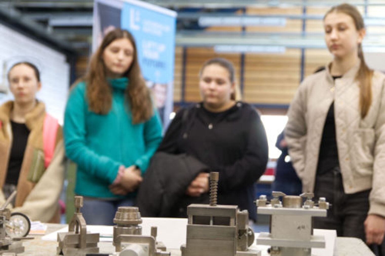 Drei Jugendliche betrachten Metallbauteile auf einem Ausstellungstisch am Metallbauer-Stand