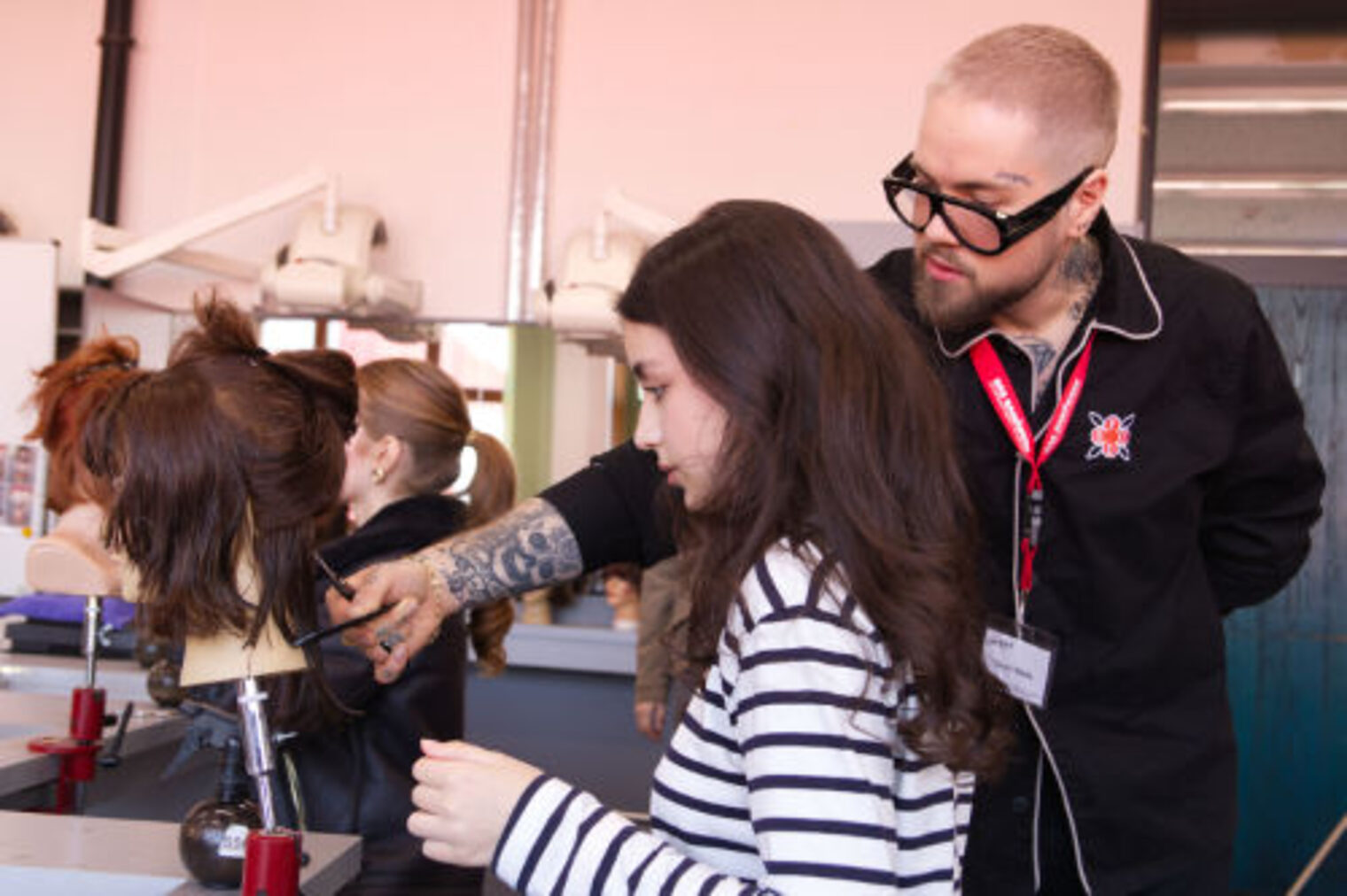 Friseur-Ausbilder zeigt einem Maedchen die Schnitttechnik an einem Uebungskopf