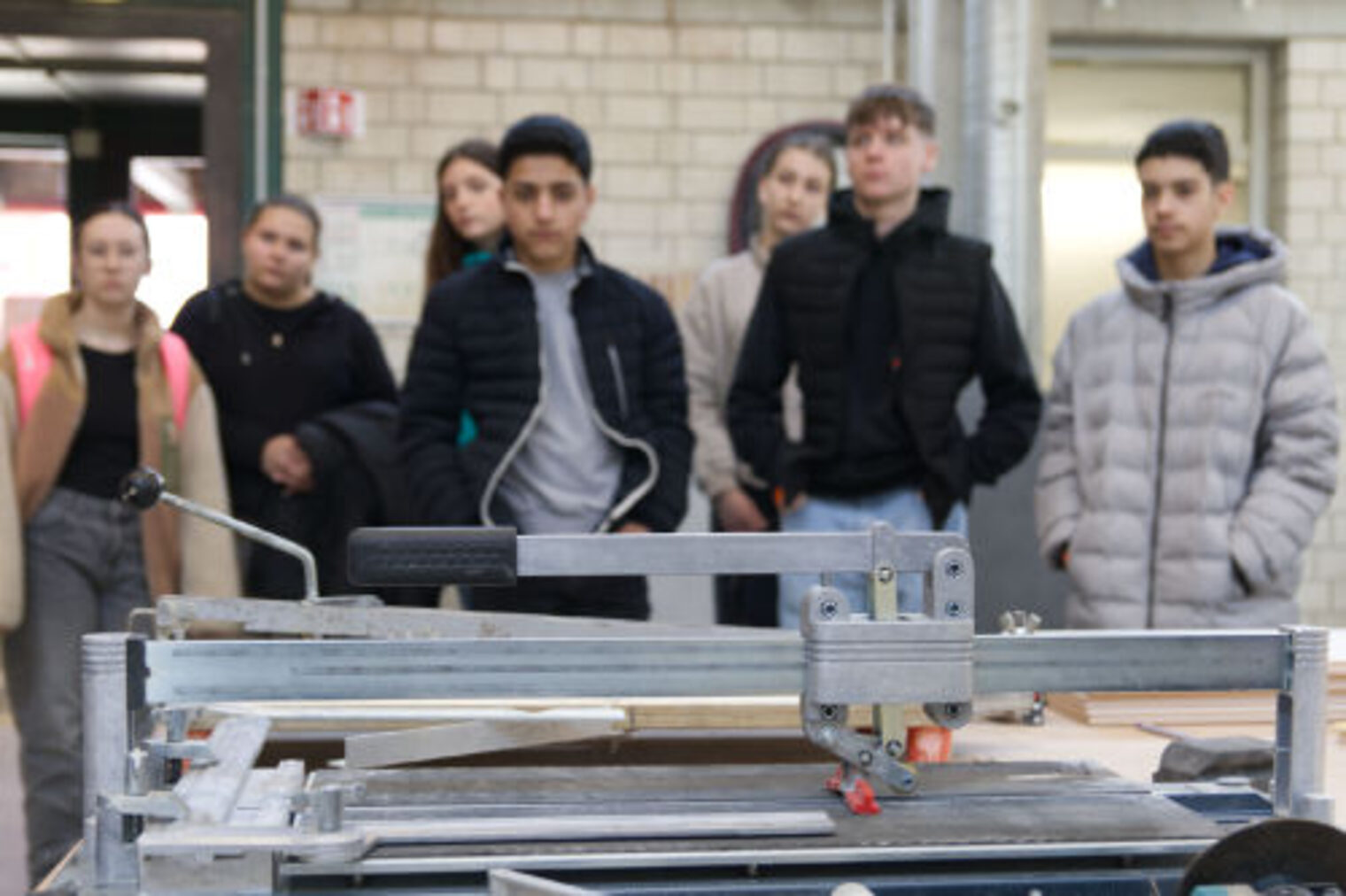 Gruppe Jugendlicher beobachtet eine Fliesenschneidemaschine im Vordergrund