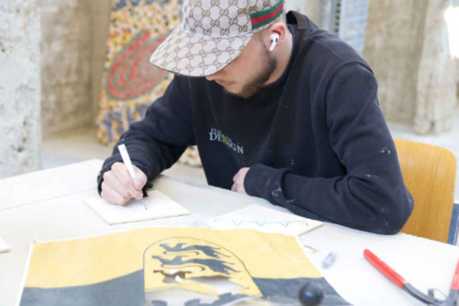 Junger Mann zeichnet ein Fliesenmuster auf Papier, im Hintergrund ein Mosaik und das Baden-Wuerttemberg-Wappen