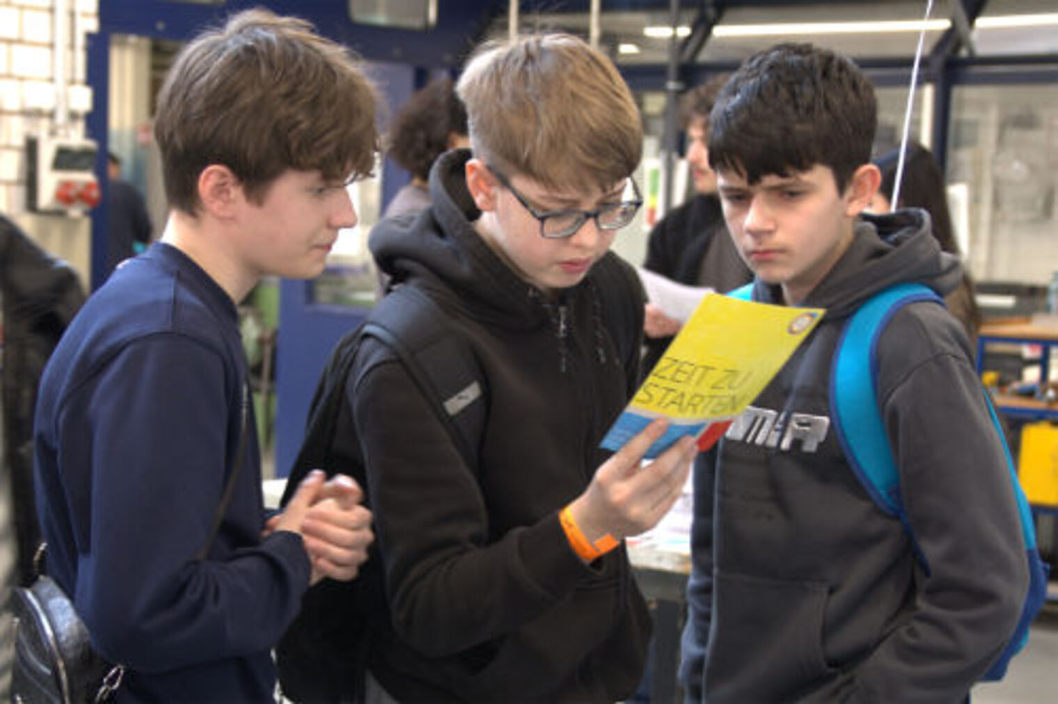 Drei Jugendliche lesen gemeinsam eine Broschuere "Zeit zu starten" am SHK-Stand