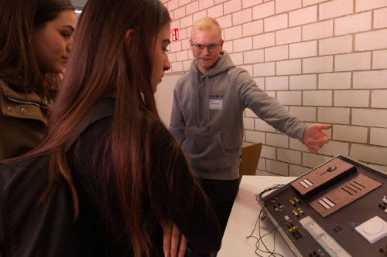Auszubildender erklaert zwei Schuelerinnen ein Elektro-Schaltpult am Messestand