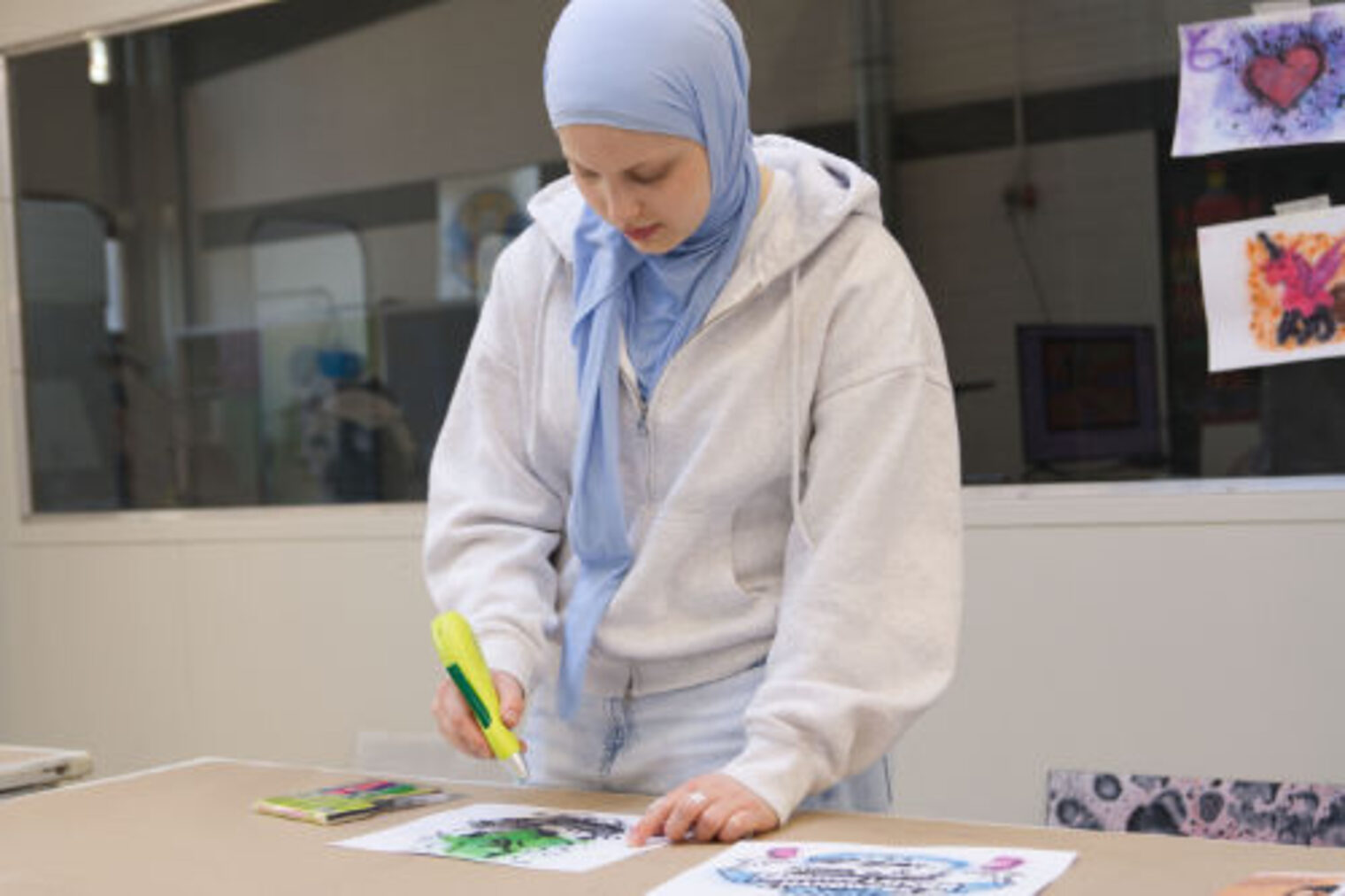 Jugendliche mit Kopftuch koloriert konzentriert ein Airbrush-Kunstwerk am Tisch