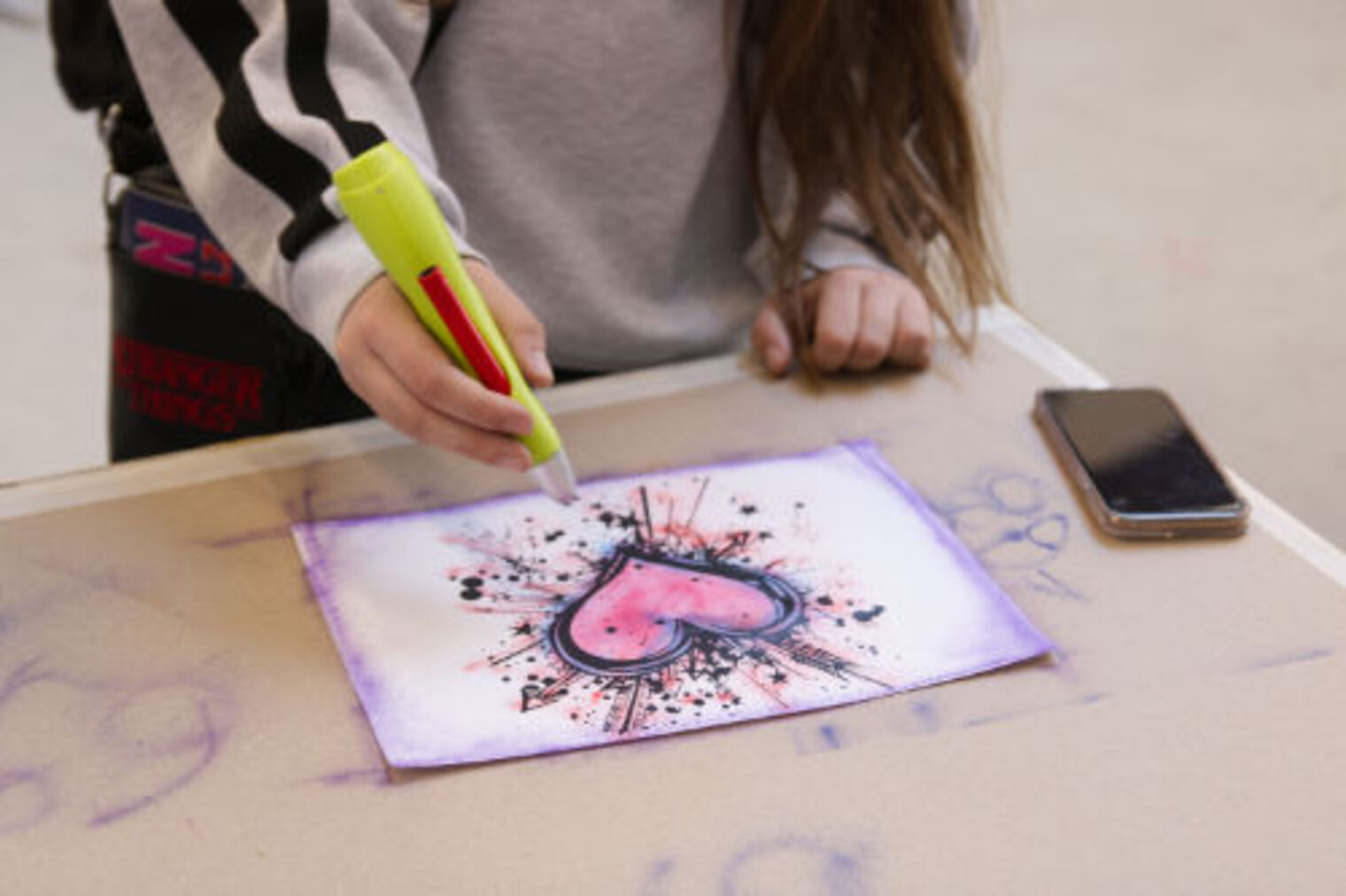 Jugendliche koloriert mit einem Airbrush-Stift ein Motiv mit Herz auf Papier