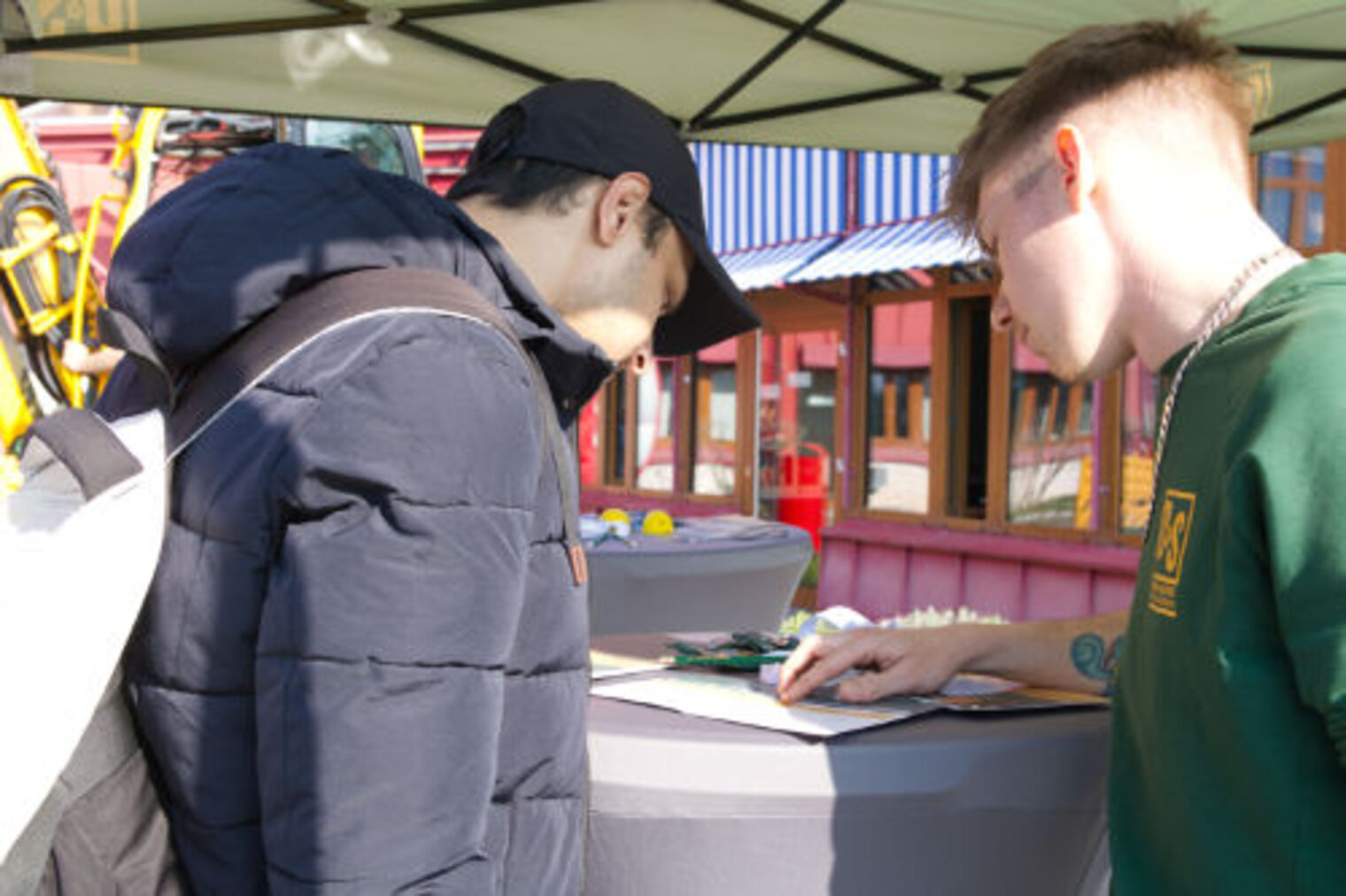 Jugendlicher und Auszubildender schauen gemeinsam auf ein Dokument an einem Infostand
