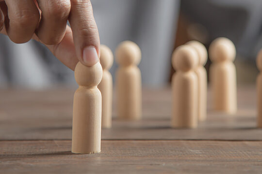 Hand die eine Holzfigur von einem Tisch anhebt, auf dem weitere Holzfiguren stehen.