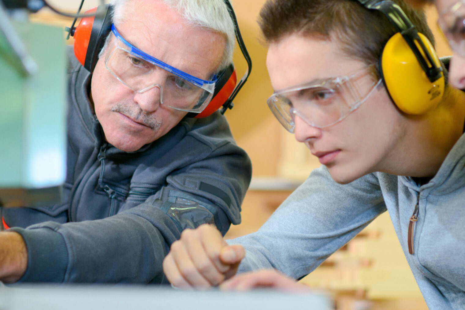 Ein Ausbilder erklärt zwei Auszubildenden etwas an einer Maschine