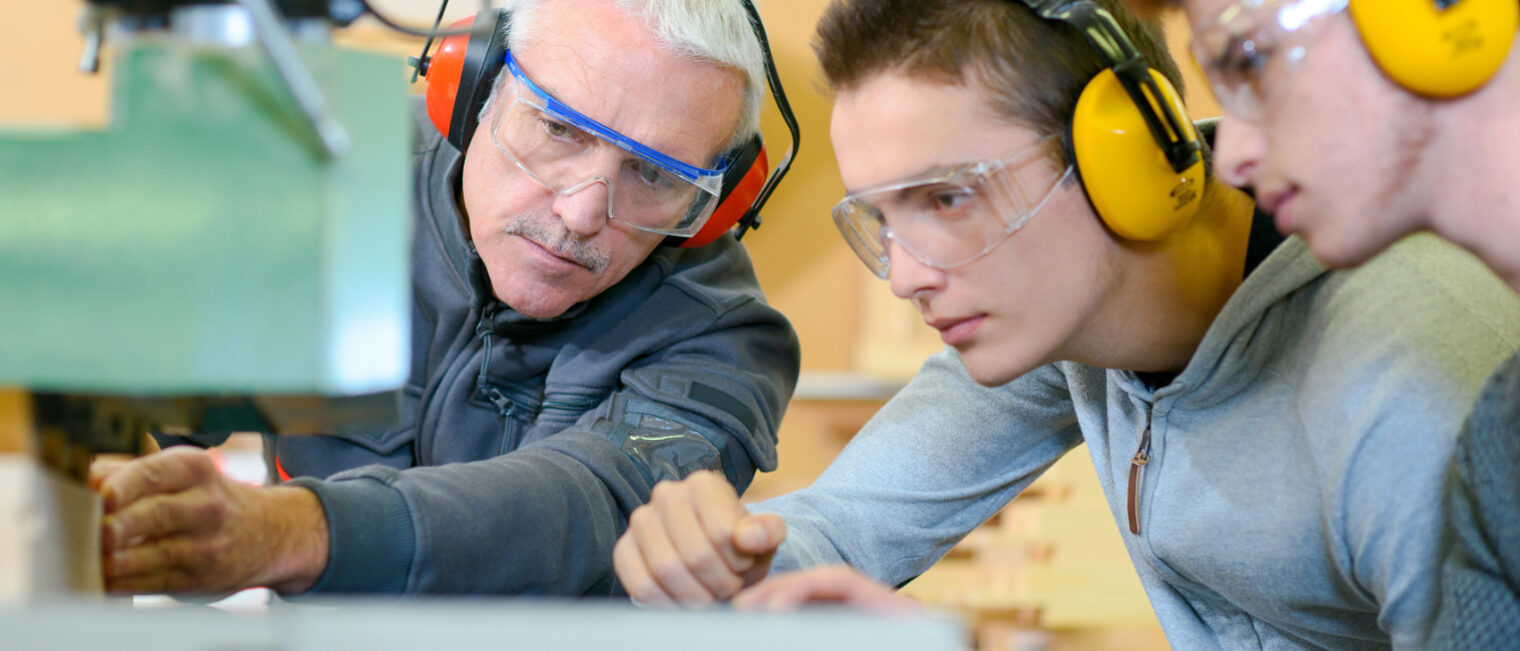 Ein Ausbilder erklärt zwei Auszubildenden etwas an einer Maschine
