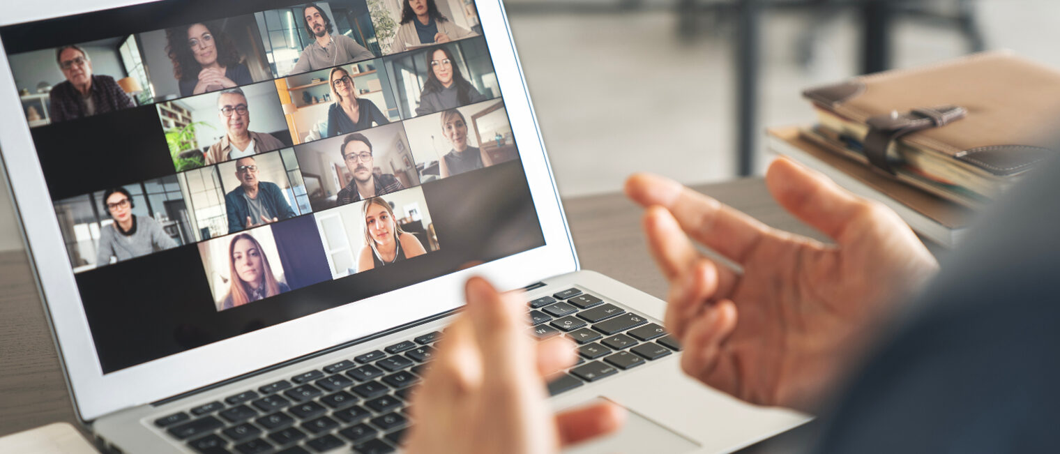 Ein Laptop auf einem Tisch mit einer Videokonferenz und einen Referenten davor.