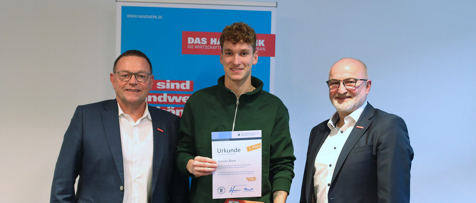 Preisübergabe, drei Männer stehen nebeneinander, der Herr in der Mitte hält sein Zeugnis und seinen Gutschein in die Kamera