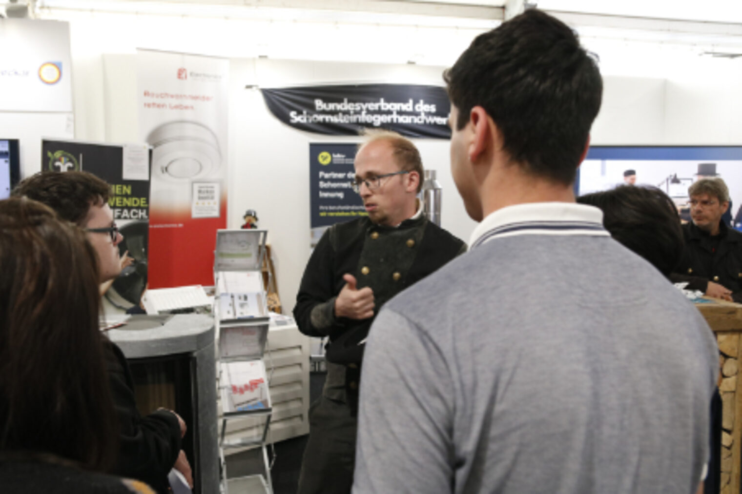 Schornsteinfeger im Zunftgewand erklaert Jugendlichen seinen Beruf am Stand der Innung des Schornsteinfegerhandwerks auf dem Maimarkt Mannheim