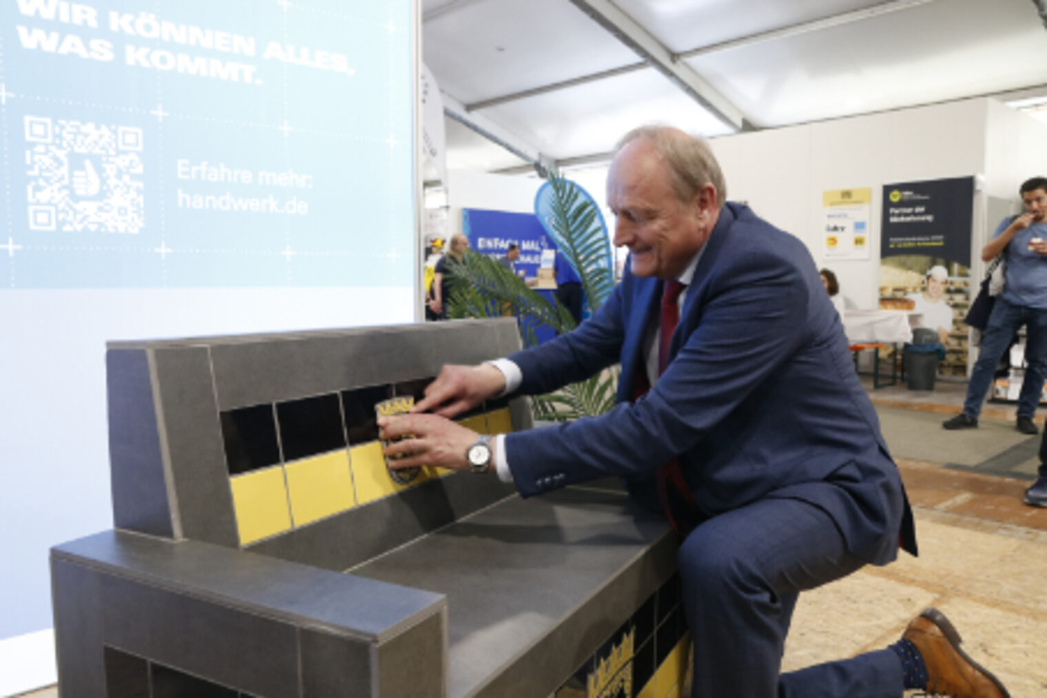 Der Präsident des Deutschen Bauernverbandes legt bei der Eroeffnung eine Fliese mit dem Baden-Württemberg-Wappen an eine geflieste Sitzbank am HWK-Stand auf dem Maimarkt Mannheim