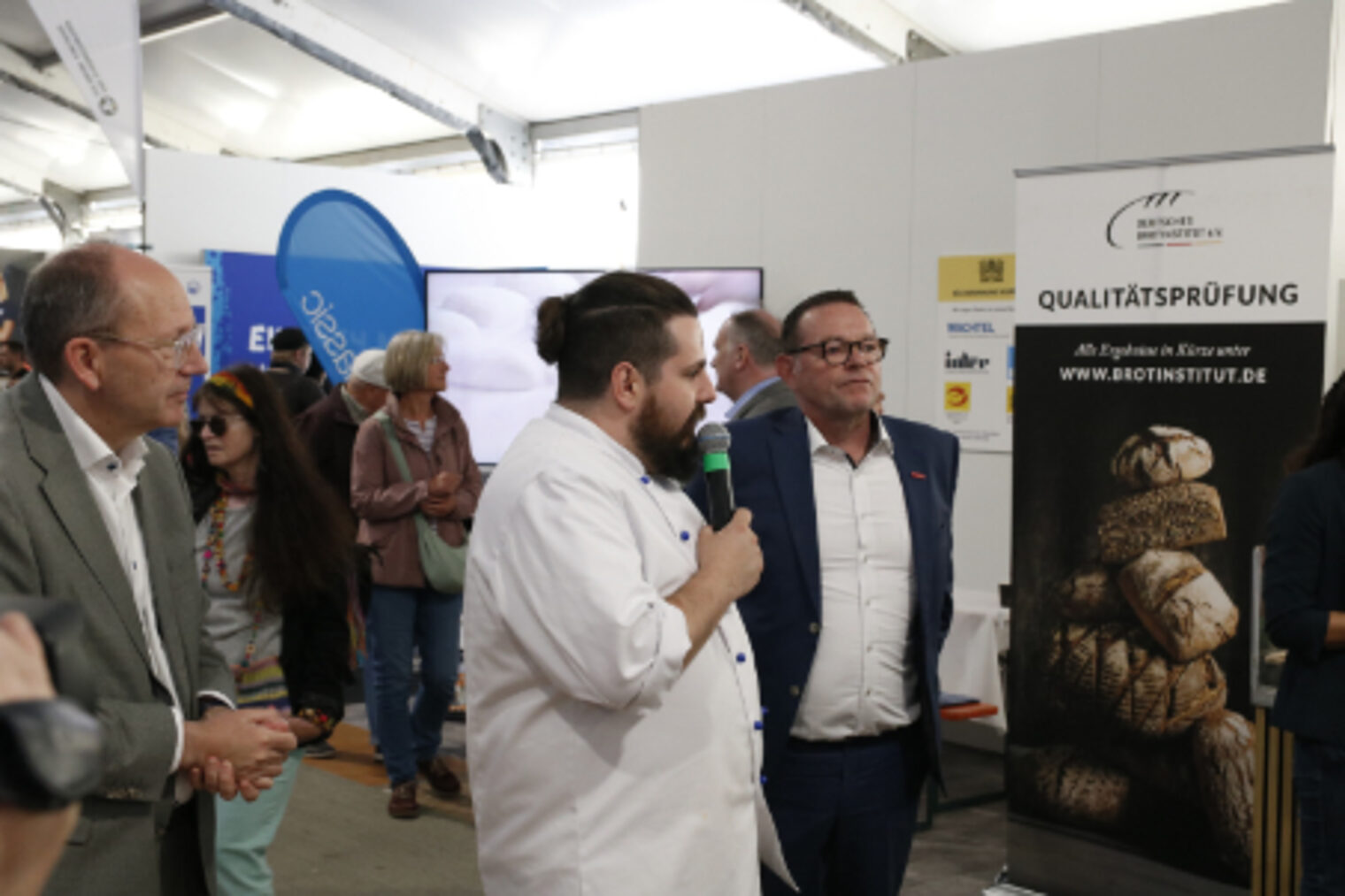 Ausbildungsmeister Florian Greiner spricht mit Mikrofon vor Besuchern am Stand der Bäcker-Innung auf dem Maimarkt Mannheim