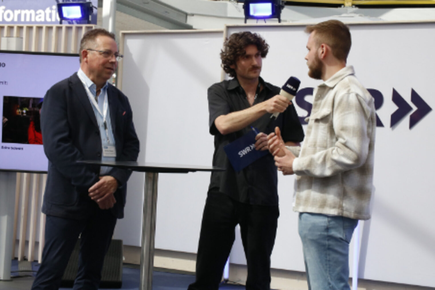 SWR-Moderator interviewt einen Azubi und Obermeister aus dem Kfz-Handwerk am SWR-Messestand auf dem Maimarkt Mannheim