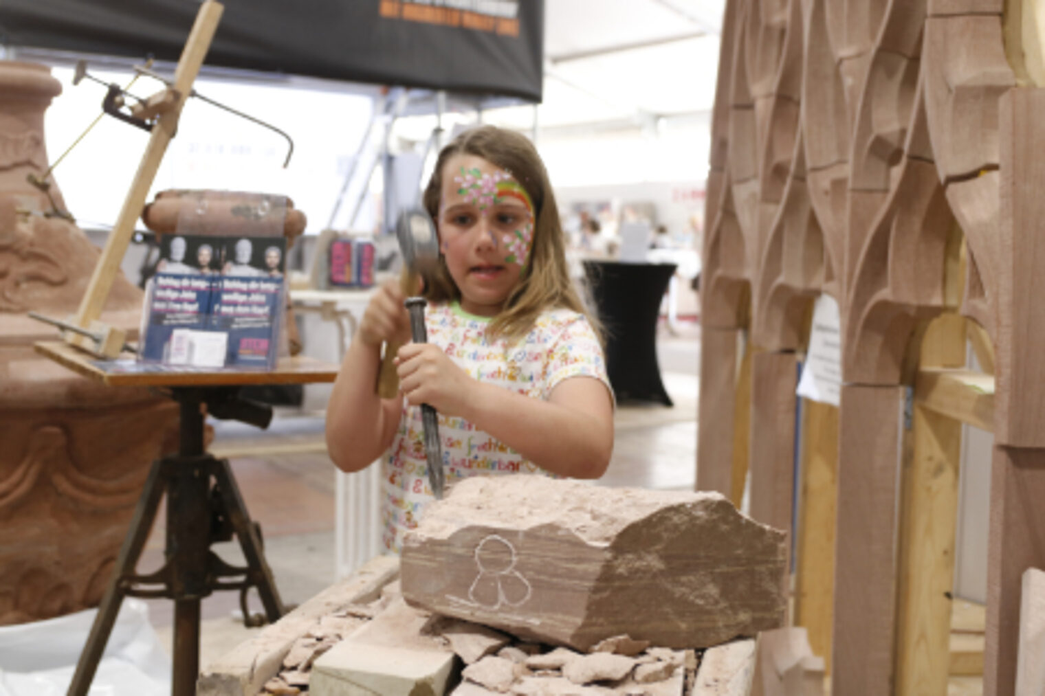 Kleines Maedchen bearbeitet mit Hammer und Meissel einen Sandsteinblock am Steinmetz-Stand auf dem Maimarkt Mannheim