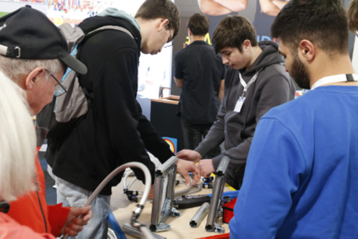 Jugendliche und ein aelterer Besucher schauen sich Sanitaerinstallations-Bauteile am SHK-Stand auf dem Maimarkt Mannheim an