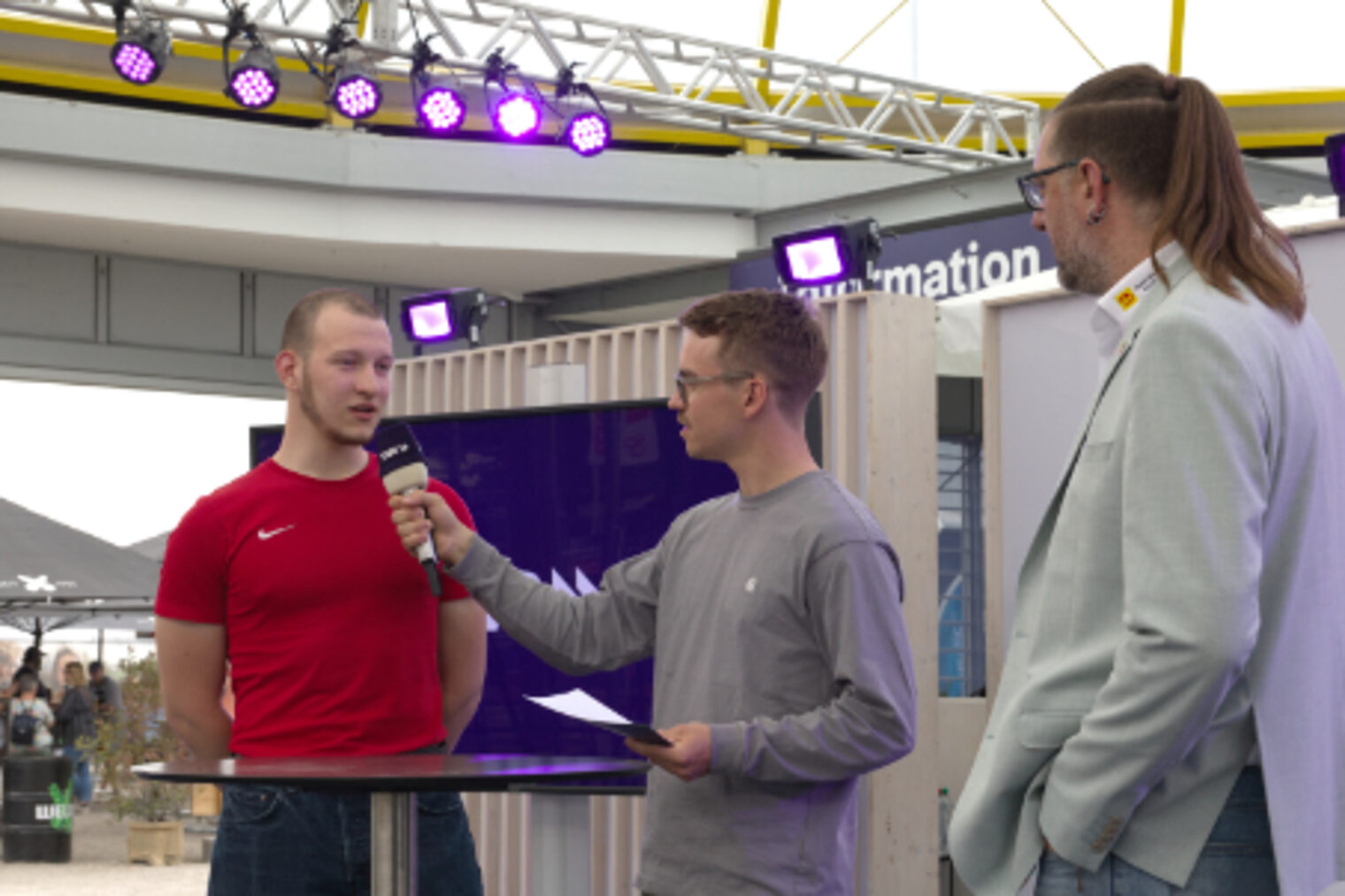 Drei Personen beim Interview am SWR-Aussenstand mit lila Beleuchtung auf dem Maimarkt Mannheim