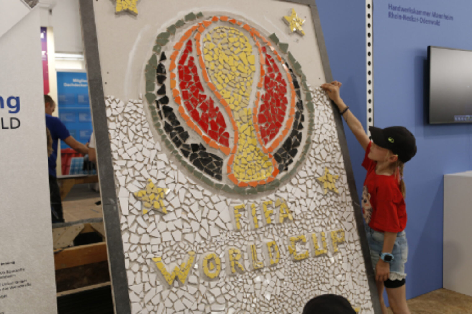Kind befestigt einen Mosaikstein am grossen FIFA-World-Cup-Mosaik am Fliesenleger-Stand auf dem Maimarkt Mannheim