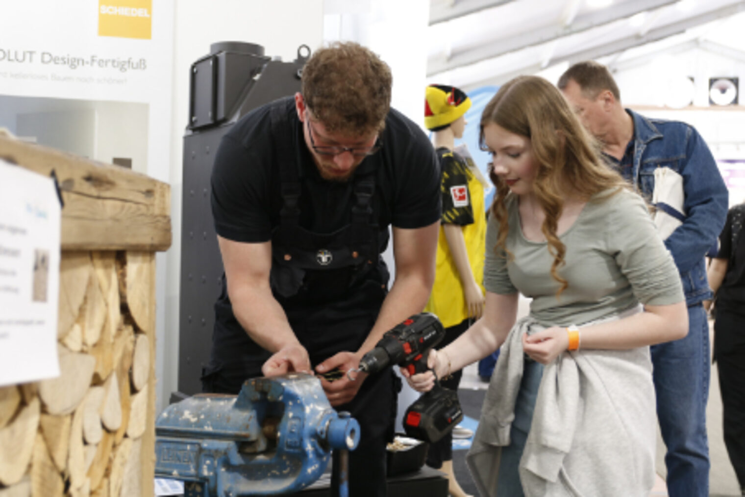 Schornsteinfeger zeigt einer jungen Frau den Umgang mit einem Bohrgerat am Stand auf dem Maimarkt Mannheim