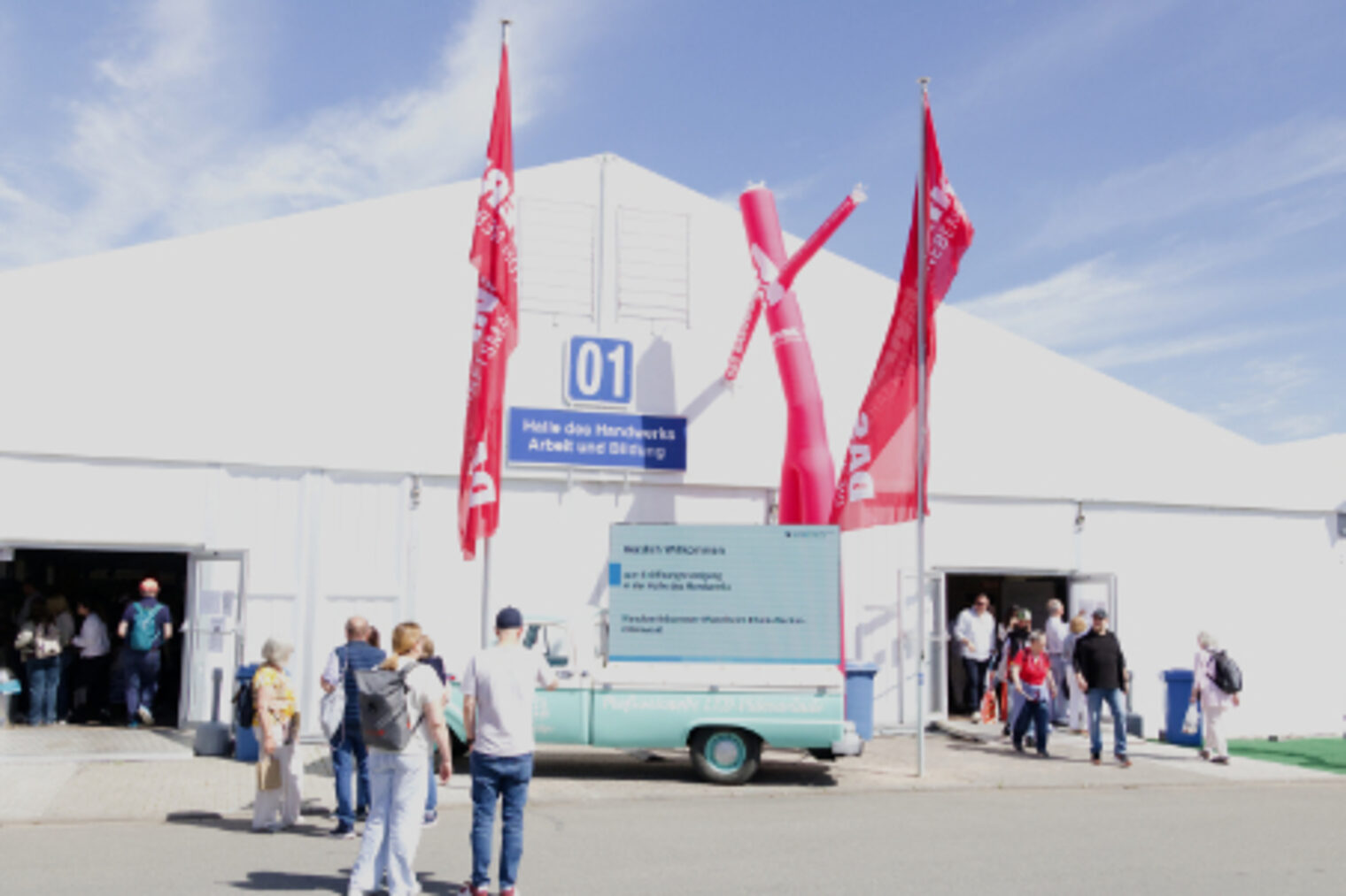 Eingang zur Halle des Handwerks - Arbeit und Bildung mit roten Fahnen und Lufttaenzern auf dem Maimarkt Mannheim