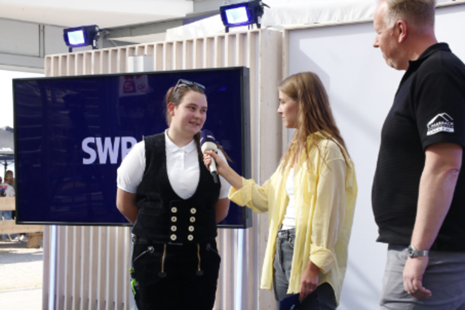 SWR-Moderatorin interviewt eine Dachdeckerin in Berufskleidung am SWR-Stand auf dem Maimarkt Mannheim