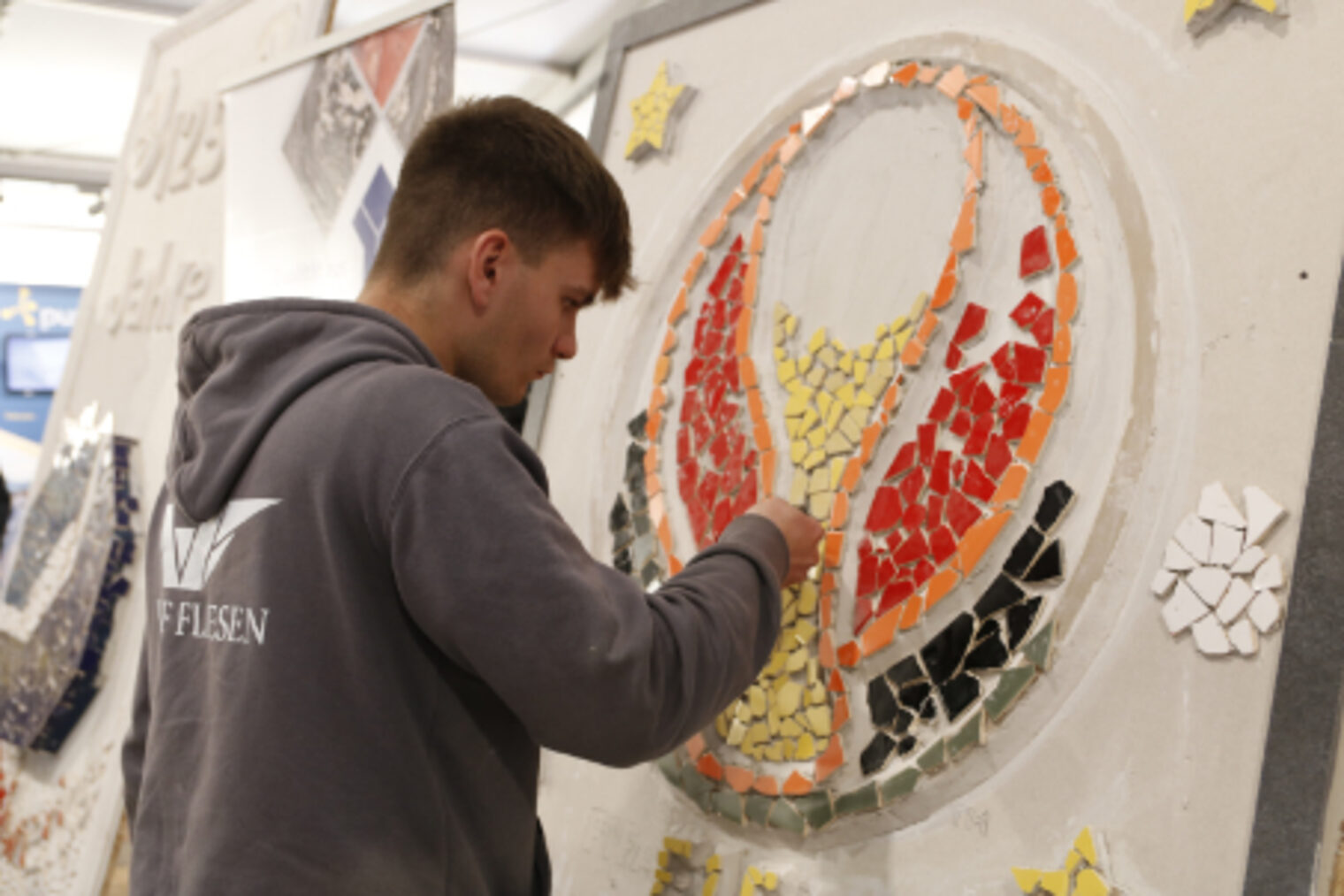 Junger Mann legt farbige Mosaikfliesen zu einem Fussball-Motiv am Fliesenleger-Stand auf dem Maimarkt Mannheim