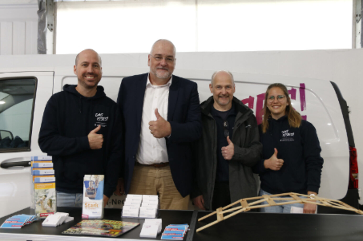 Vier Personen posieren laechelnd mit Daumen hoch vor einem Transporter am Stand Das isses! auf dem Maimarkt Mannheim