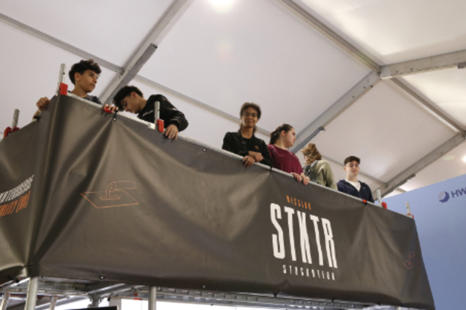 Jugendliche stehen auf einer erhoehten Plattform Mission Stukko Stuckateur am HWK-Stand auf dem Maimarkt Mannheim