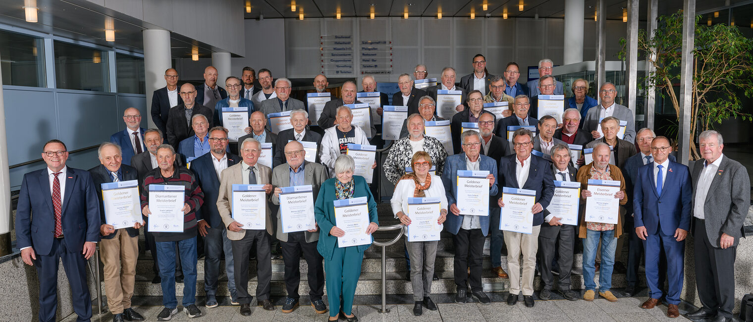 Große Gruppe von Senioren in einer Festsaal-Aula, jeweils mit Ehrenurkunden in den Händen